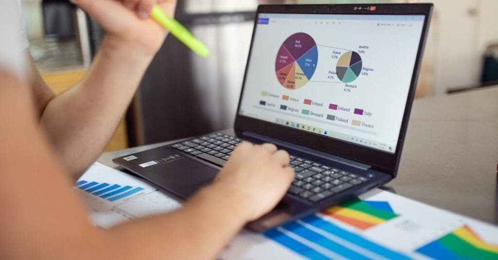 Person analyzing financial charts and graphs on a laptop with colorful documents, showcasing market analysis.